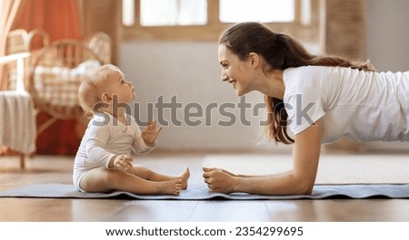 Side view of cheerful sporty young mother exercising with her little baby toddler at home. Mom doing regular workout planking on fitness mat with cute blonde infant son, panorama