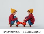 Side view of cheerful twin brothers wearing similar shirts and jeans relaxing on skateboards on white background and looking at each other