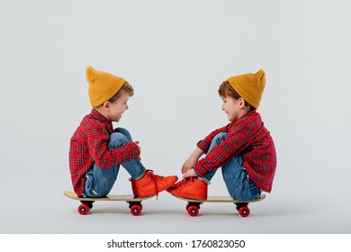 Side view of cheerful twin brothers wearing similar shirts and jeans relaxing on skateboards on white background and looking at each other - Shutterstock ID 1760823050
