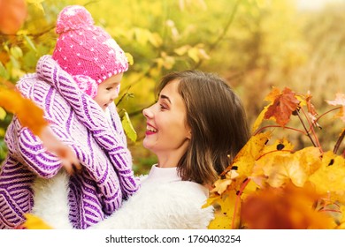 Side View Of Cheerful Young Woman Lifting And Playing With Baby In Warm Clothes On Weekend Day In Autumn Park