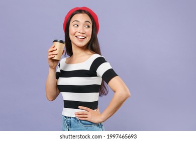 Side view cheery young brunette asian woman 20s in striped t-shirt red beret stand hold takeaway delivery craft paper brown cup coffee to go isolated on pastel violet colour background studio portrait - Powered by Shutterstock