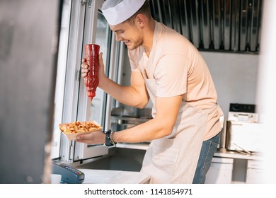 side view of chef adding ketchup to hot dog in food truck