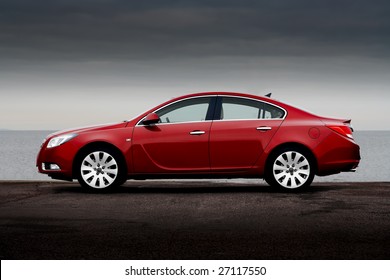 Side view of cherry red business sedan parked on a sea coast