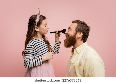 Side view of child in crown headband holding makeup brush near father isolated on pink - Powered by Shutterstock