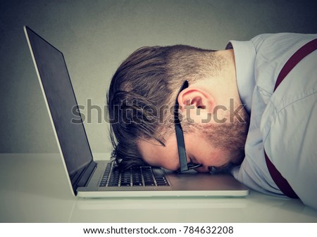 Side view of chubby man looking broken while lying on top of laptop. 
