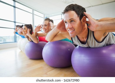 Side view of class exercising on fitness balls in a row at the bright gym