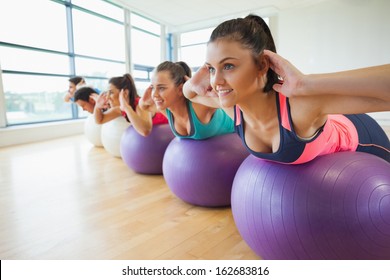 Side view of class exercising on fitness balls in a row at the bright gym
