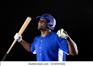 Side view close up of an African American male baseball player, a hitter wearing a team uniform, a helmet and holding a baseball bat, with fist raised in celebration of a victory  - Powered by Shutterstock