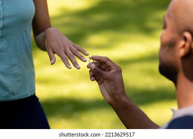 Side view close up of an African American man kneeling in the garden, proposing to his mixed race female partner and presenting her with an engagement ring - Powered by Shutterstock