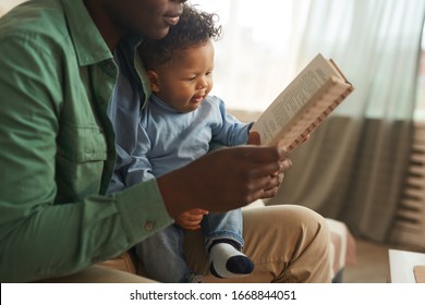 Side View Close Up Of Caring African-American Dad Reading Book To Cute Baby Son At Home, Copy Space