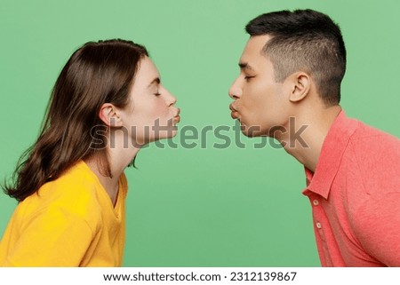 Side view close up caucasian young couple two friends family man woman 20s wear basic t-shirts together going to kiss each other isolated on pastel plain light green color background studio portrait