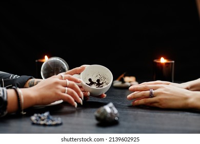 Side View Close Up Of Female Fortune Teller Reading Coffee Grounds Telling Destiny In Seance With Young Woman In Dark