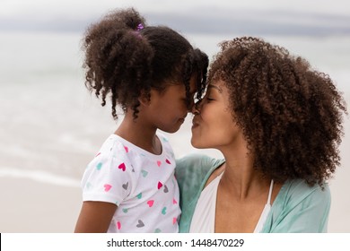 Side view close up of happy young mixed-race mother and daughter rubbing noses at beach on a sunny day.
