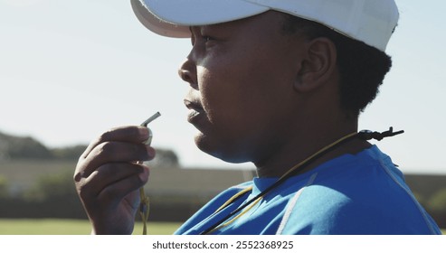 Side view close up of a middle aged biracial female rugby coach standing on a sports field blowing a whistle - Powered by Shutterstock