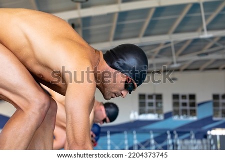 Side view close up of multi-ethnic group of male swimmers at swimming pool, standing on starting blocks before the race, bending down ready to plunge into water