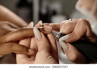 Side view close up of nail tech carefully preparing female clients hands for manicure using electric nail drill in salon - Powered by Shutterstock