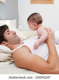 Side View Close Up Portrait Of A Young Father Holding His New Born Baby Daughter On His Chest While Laying Down On A Bed At Home, Enjoying Quality Time Together.