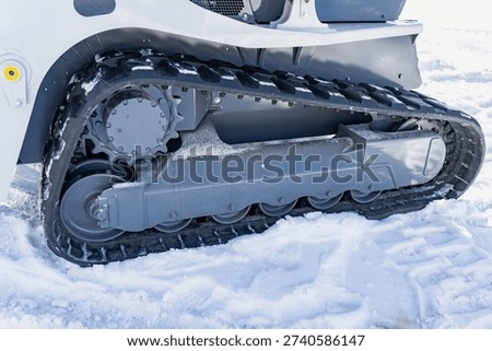 Side view close up of rubber track undercarriage on compact construction loader in snow, showing sprocket, rollers and track frame in winter