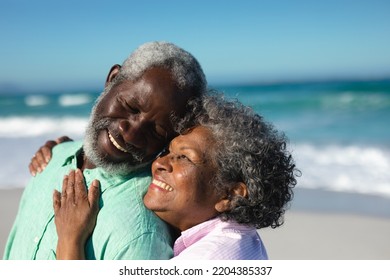 Side view close up of a senior African American couple standing on the beach with blue sky and sea in the background, embracing and smiling at each other - Powered by Shutterstock