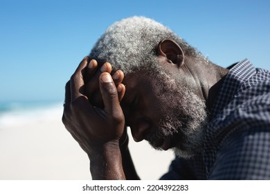 Side view close up of a senior African American man sitting on the beach with blue sky in the background, holding his head and thinking - Powered by Shutterstock