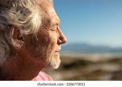 Side view close up of a senior Caucasian man at the beach in the sun, smiling with eyes closed, against a blue sky - Powered by Shutterstock