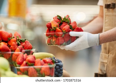 Side view close up of unrecognizable man holding box of delicious fresh strawberries at fruit and vegetable stand in farmers market, copy space