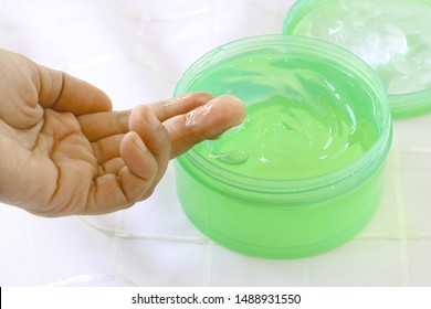 Side View Of Close Up Woman Finger Applying Green Gel Cream (aloe Vera Gel) In Plastic Container On White Fabric Background