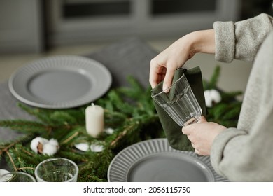 Side view close up of young woman setting up plates on dining table decorated for Christmas with fir branches and candles in grey tones, copy space