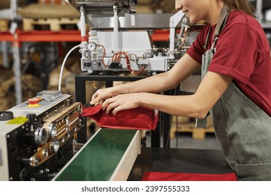 Side view close up of young woman sealing plastic bags while working on packaging line in food factory workshop - Powered by Shutterstock