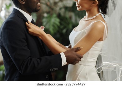 Side view closeup of black young couple getting married with bride adjusting jacket and boutonniere before wedding ceremony