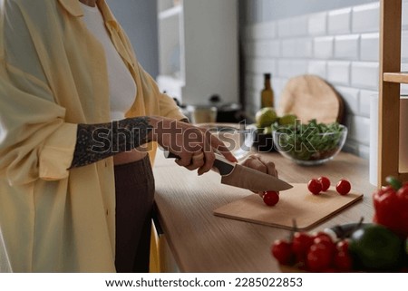 Side view closeup of pregnant woman cooking healthy meal and cutting vegetables in kitchen