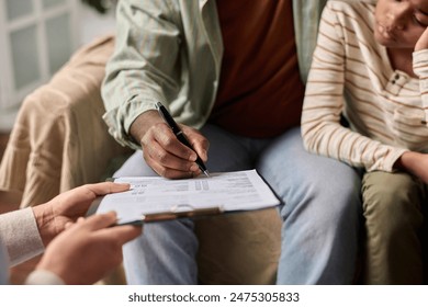 Side view closeup of unrecognizable Black man signing document on clipboard in clinic copy space