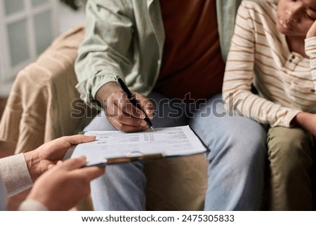 Side view closeup of unrecognizable Black man signing document on clipboard in clinic copy space