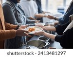 Side view closeup of unrecognizable volunteer giving hot meals to refugees in line at help center with focus on hands holding plate of rice