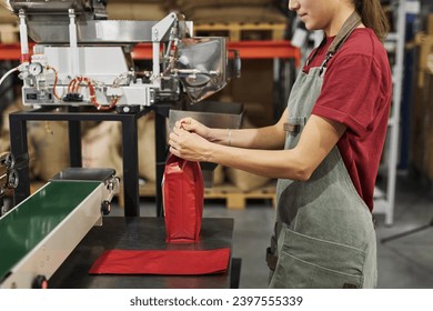 Side view closeup of young woman packaging coffee bags at production line in small food factory workshop, copy space - Powered by Shutterstock