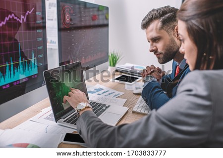 Side view of computer systems analysts using charts on computer monitors while working in office