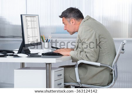 Side view of concentrated businessman using computer at desk in office
