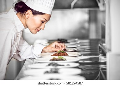 Side view of a concentrated female chef garnishing food in the kitchen