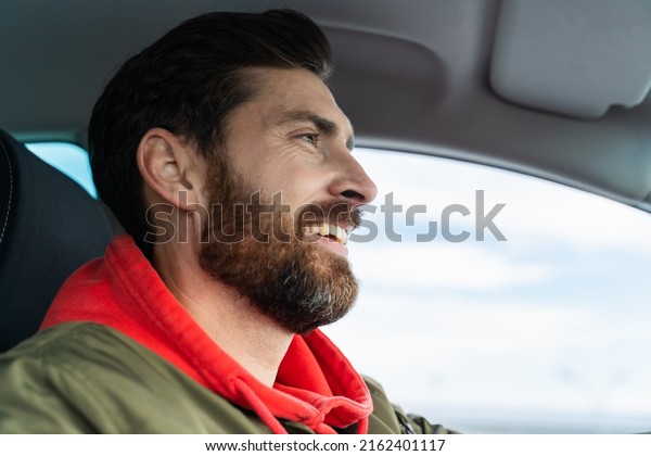 Side view of the concentrated guy keeping tool for\
driving car. He locating in cabin on seat of driver and looking at\
the road 