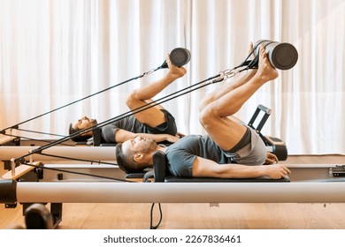 Side view of concentrated male athletes in sportswear performing pilates hip mobility exercise on reformer during workout - Powered by Shutterstock