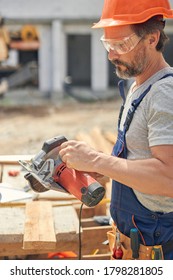 Side View Of A Concentrated Male Builder In Safety Goggles Staring At A Circular Saw