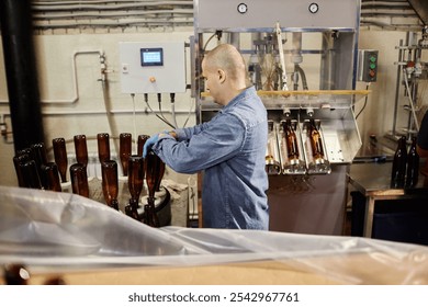 Side view of concentrated male production operator carefully sterilizing glass bottles while directing cleaning machine in workshop of cider or beer factory, copy space - Powered by Shutterstock