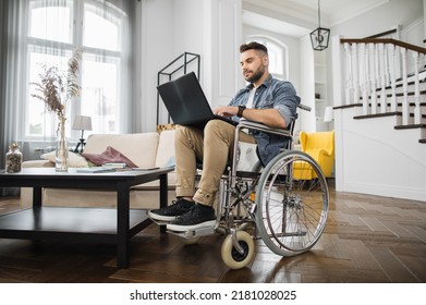 Side View Of Concentrated Young Man In Wheelchair Typing On Wireless Laptop In Bright Living Room. Caucasian Male Employee With Disability Working At International Company From Home.