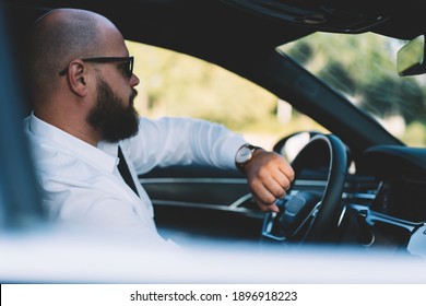 Side View Of Confident Male Driver Sitting In Automobile With Wristwatch On Hand While Commuting To Work During Warm Weather