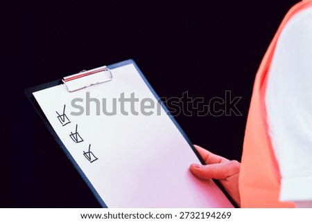 Side view of construction worker in orange vest examining clipboard with marked checklist items.