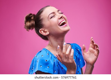 Side view of contented laughing softly female with closed eyes. Trendy girl with two buns isolated over pink background 