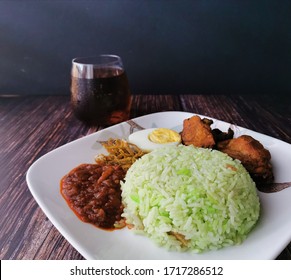 Side View Of A Malay fragrant rice dish Cooked In coconut Milk and pandan Leaf Called Nasi Lemak. Served With Chilli Sauce Called Sambal And Fried Anchovies, Boiled Egg, And Fried Chicken. 