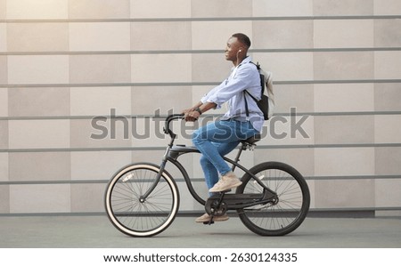 Side view of cool black guy with earphones racing on his bicycle near brick wall downtown