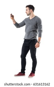 Side View Of Cool Relaxed Young Casual Man Taking Picture With Mobile Phone. Full Body Length Portrait Isolated Over White Studio Background.