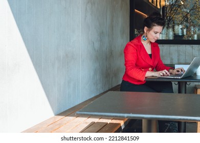 Side View With Copy Space Of Young Caucasian Business Woman, Wearing Red Casual Clothes, Sitting In A Restaurant, Working With Her Laptop.